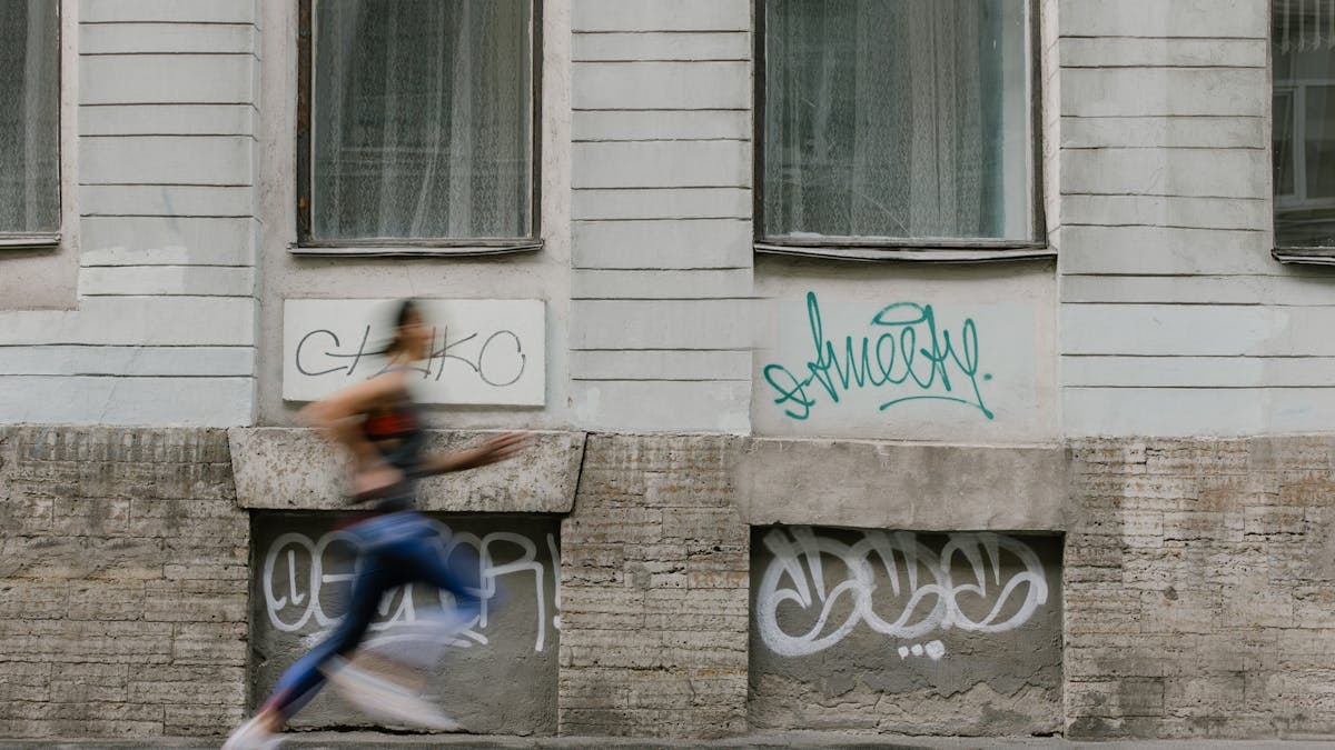 Blurred motion of a woman running past a graffiti-covered urban wall. Captures dynamic energy.
