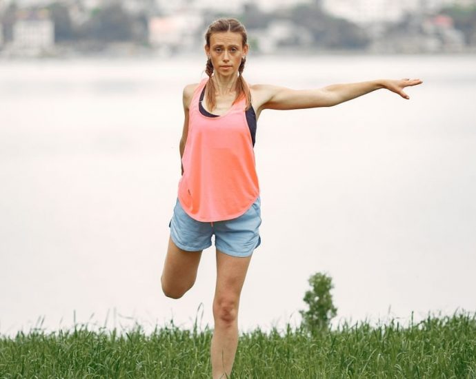 Woman exercising and stretching by a lakeside in a peaceful outdoor setting.