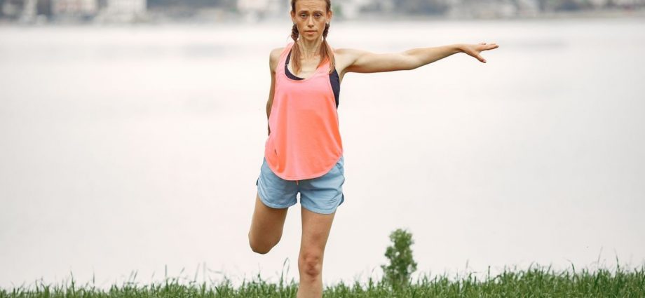 Woman exercising and stretching by a lakeside in a peaceful outdoor setting.